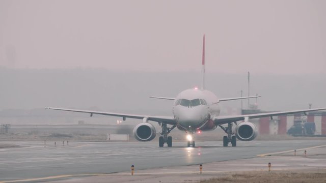 The Superjet 100 moving on a taxiway in the airport in a rainy day. Some airport facilities in the background