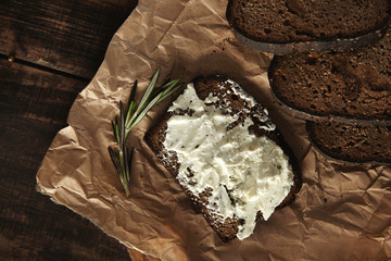 Top view, sandwich with rustic bread and soft goat cheese with herbs near slices of homemade luxury rye bread with figs and rosemary spice on craft paper on wooden table