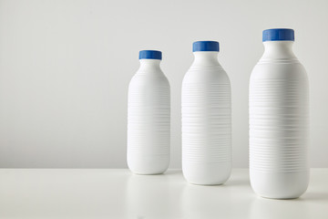 Three blank white plastic riffled bottles with blue caps in row isolated on table Space for your text on side Merchandise retail set, rich texture