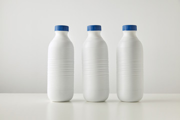 Three blank white plastic riffled bottles with blue caps in row isolated on table in center Space for your text Merchandise retail set, rich texture