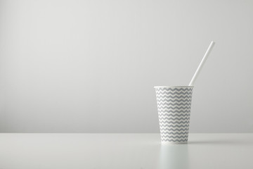 one paper cup decorated with gray black line pattern and with white drinking straw inside isolated on table Place for your text above