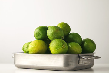  Closeup of fresh limes in a steel saucepan isolated on the white table. Free space for text