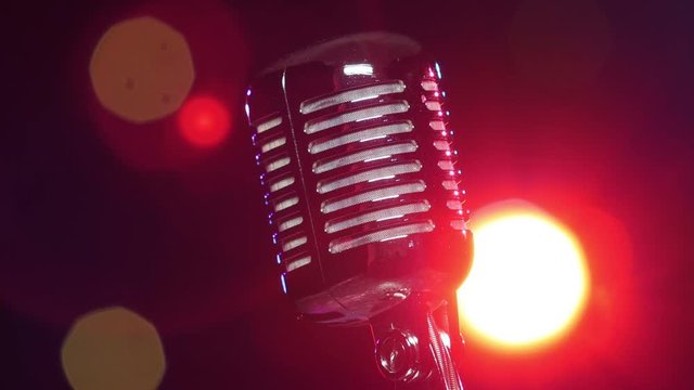 Retro shiny microphone slow rotating against blurry flashing lights