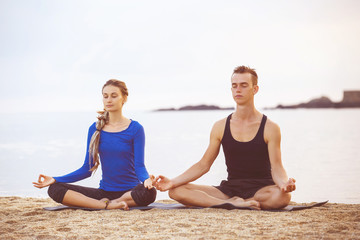 Young couple is practicing yoga at golden sea sunrise background