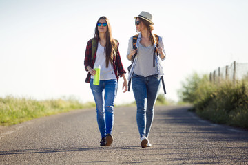 Two beautiful ladies hikers walking on the road. - obrazy, fototapety, plakaty