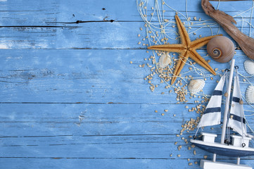 Décoration maritime sur fond de bois bleu avec un bateau en bois, une étoile de mer, des coquillages, du bois flotté et un filet de pêche