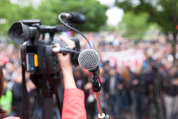 Microphone in focus against blurred crowd. Filming protest.