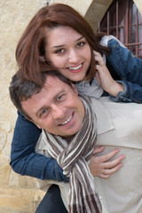 Man giving piggy back to woman, woman holding her cell phone
