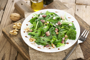 Feldsalat mit Speckwürfeln und Walnüssen auf weißem Teller angerichtet