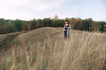 Pregnant woman in black dress and dreadlocks on the background of wild nature