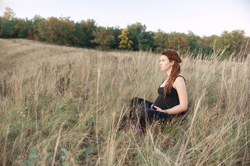 Naklejka na ściany i meble Pregnant woman in black dress and dreadlocks on the background of wild nature