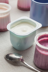 Obraz na płótnie Canvas Yogurts assortment in plastic bowls on light cloth background. Natural and fruit healthy, diet, gourmet dessert for granola breakfast. Sweet yoghurts closeup.