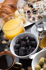 Breakfast assorted yoghurt, granola, coffee, juice, croissant, olives. Appetizer mix with morning dishes. Healthy, fresh, delicious food on dark background. Top view. Copy space.