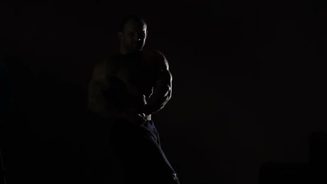 Professional bodybuilder flexing muscles in darkness, boasting of masculine body