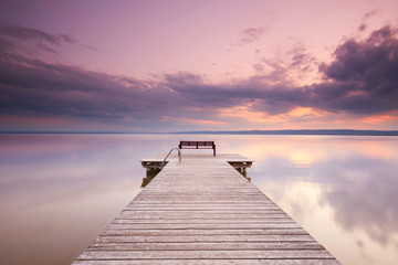 Fototapeta na wymiar alter Holzsteg mit Bank am See zum Sonnenuntergang