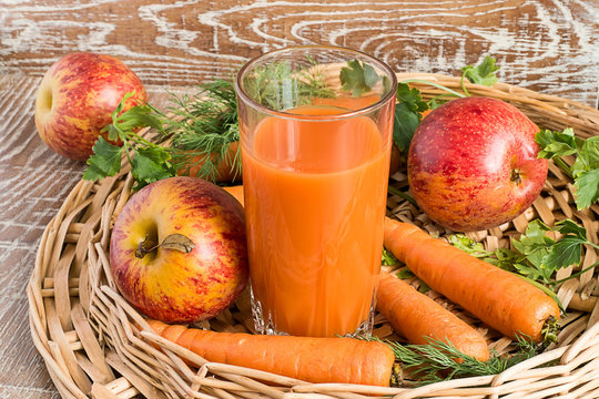 Juice, apples and carrots.    A glass with juice, fresh apples and carrots in a wicker basket on a brown wooden background.