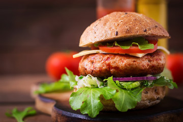 Big sandwich - hamburger with juicy chicken burger, cheese, tomato, and red onion on wooden background