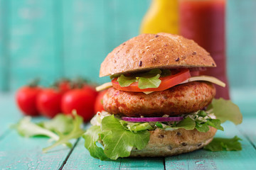 Big sandwich - hamburger with juicy chicken burger, cheese, tomato, and red onion on wooden background
