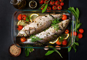 Two baked seabass in a baking dish with spices on an black background. Top view