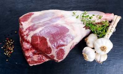 Raw lamb leg on blue stone background with herbs