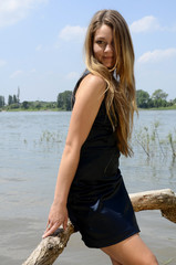 Naklejka premium Junge hübsche Frau mit langen braunen Haaren in blauen Minikleid an Flussufer
