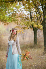 A girl in a long dress, boho style. At the head of the model wreath in the hands of an autumn bouquet. Copy space.