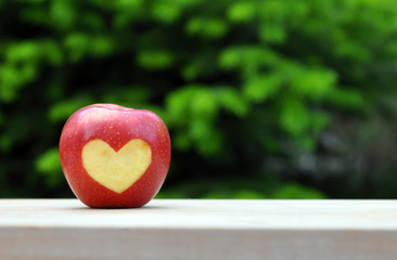 Red Apple With Heart Symbol On Wood Table Over Nature Background