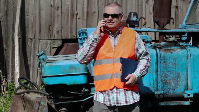 Worker talking on smart phone near tractor