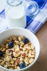 Close view of healthy breakfast on a wooden table. Muesli in a white bowl. Oats with nuts and blueberries. Glass of milk. Vertical view. Selective focus.