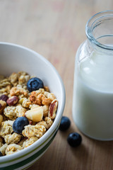 Close view of healthy breakfast on a wooden table. Muesli in a white bowl. Oats with nuts and blueberries. Glass of milk. Vertical view. Selective focus.