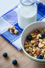 Close view of healthy breakfast on a wooden table. Muesli in a white bowl. Oats with nuts and blueberries. Glass of milk. Vertical view. Selective focus.