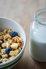 Close view of healthy breakfast on a wooden table. Muesli in a white bowl. Oats with nuts and blueberries. Glass of milk. Vertical view. Selective focus.