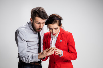 Business concept. The two young colleagues holding mobile phone on gray background