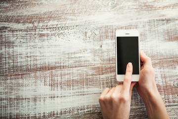 Hand holding White Smartphone with blank screen on wood backgrou