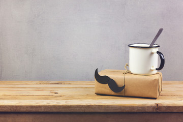Retro coffee cup and gift box with paper mustache on wooden table. Father's day holiday concept...