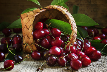 Red cherries poured out of a wicker basket, vintage wooden backg