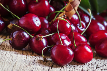 Red cherries poured out of a wicker basket, vintage wooden backg