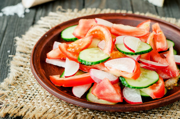 
healthy salad with fresh ripe summer vegetables , tomato, cucumber , radishes , spices and white toast on a wooden background