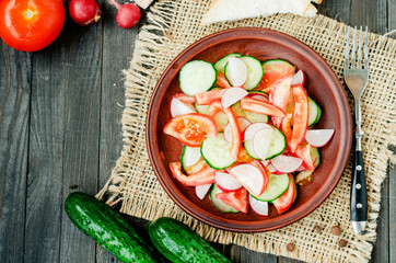 
healthy salad with fresh ripe summer vegetables , tomato, cucumber , radishes , spices and white toast on a wooden background