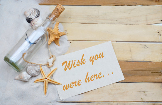 Summertime image with beachy theme of clean white sand scattered on boardwalk planks with starfish, seashells and a message in a bottle making a left side border with message tag.