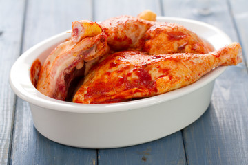 marinated chicken legs on white dish on blue wooden background