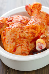 marinated chicken legs on white dish on brown wooden background