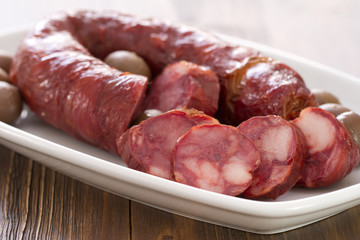 smoked portuguese sausage chourico in white dish on brown wooden background