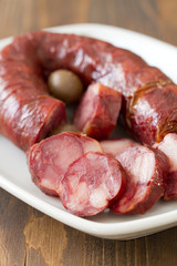 smoked portuguese sausage chourico in white dish on brown wooden background