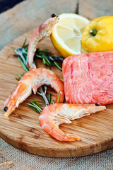 Raw salmon and shrimps with rosemary and lemon on the wooden board