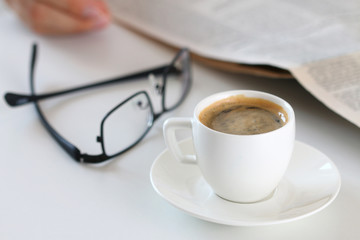 Cup of morning coffee on worktable with glasses and newspaper