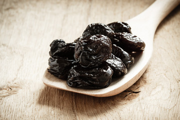 dried plums prunes on wooden spoon