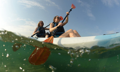 Two young women paddling blue kayak - obrazy, fototapety, plakaty