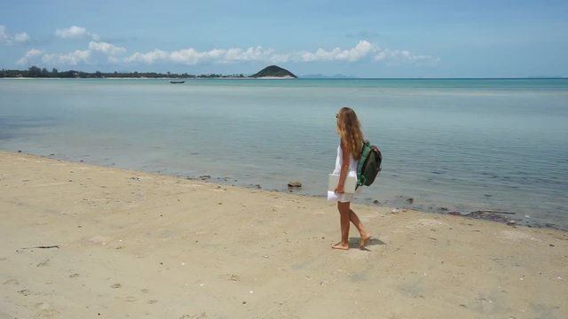 Young woman with a laptop in hand walking on a tropical beach in Koh Samui