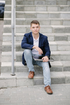 Portrait of a young businessman sitting with notebook on stairs.